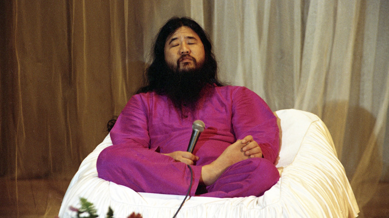 shoko asahara sitting on cushion holding microphone