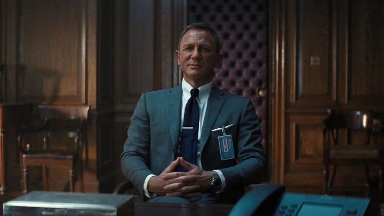 Daniel Craig's James Bond smirking while sitting in a chair in No Time to Die