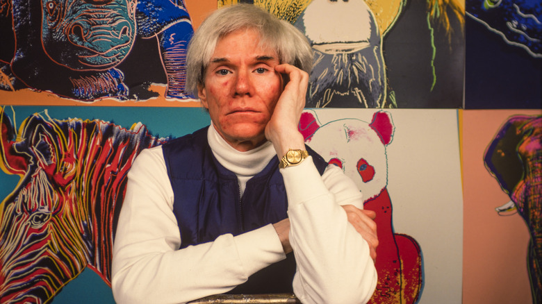 Andy Warhol sitting in front of his paintings