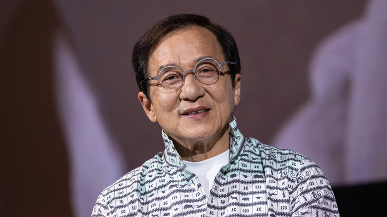 Jackie Chan smiling and wearing glasses in 2025