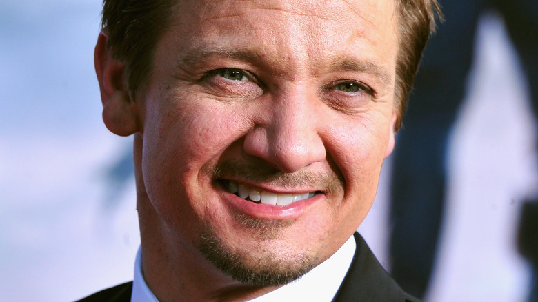 Jeremy Renner in a suit, smiling for the cameras at an event