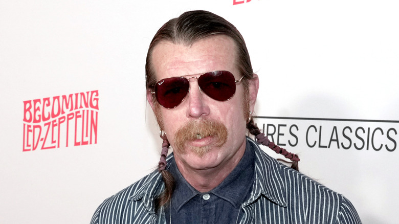Jesse Hughes in striped suit and sunglasses staring into camera