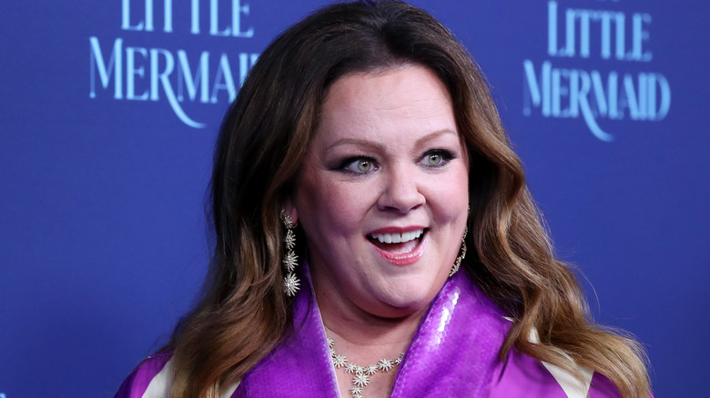 Melissa McCarthy in purple dress and smiling and looking off