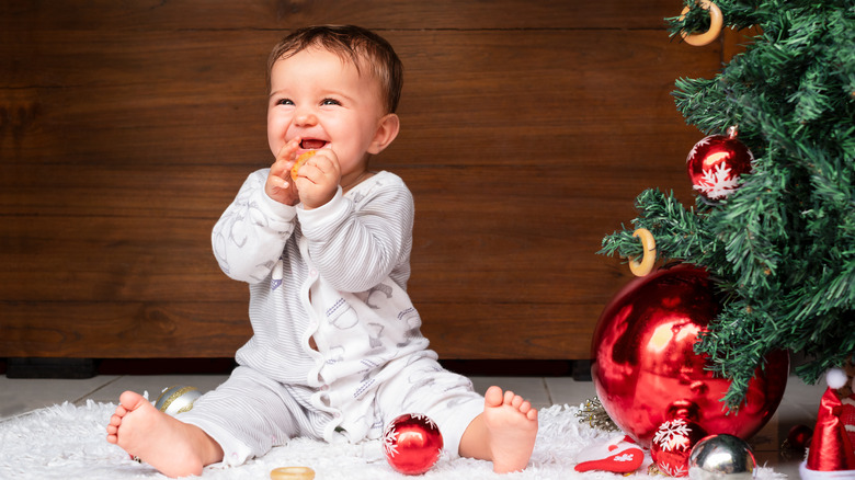 cute baby sits on the floor near the Christmas tree on a wooden background. baby eating a bagel