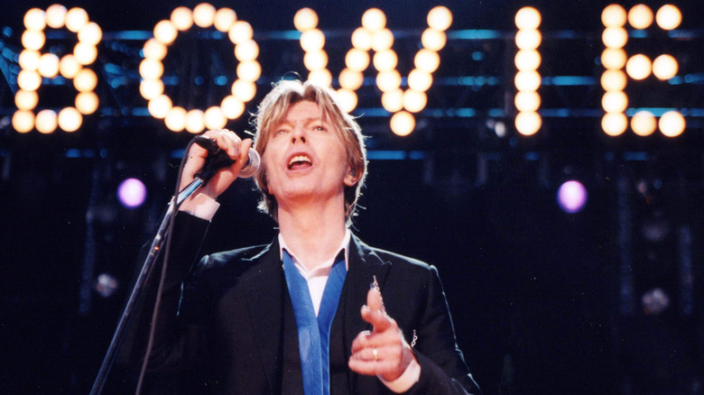 David Bowie onstage singing into a microphone in front of his name in lights