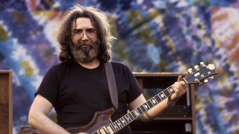 Jerry Garcia playing guitar in front of a tie-dye background