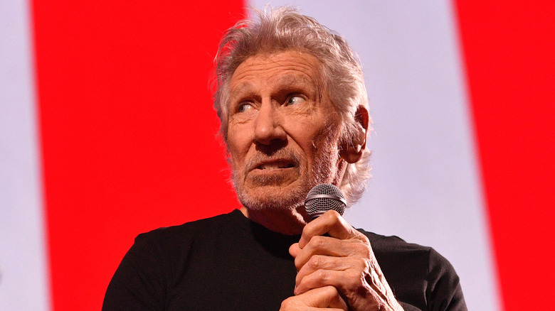 Roger Waters holding a microphone in front a a red and white background