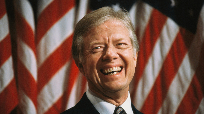 Jimmy Carter standing in front of the American flag, smiling