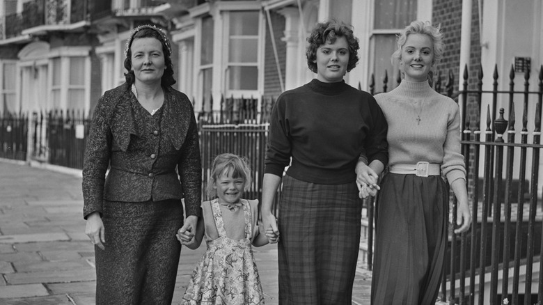 Marie Killick in smart dress stood outside in street with her three daughters