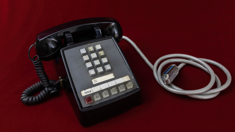 Old-fashioned black touchtone phone with grey cable on red background