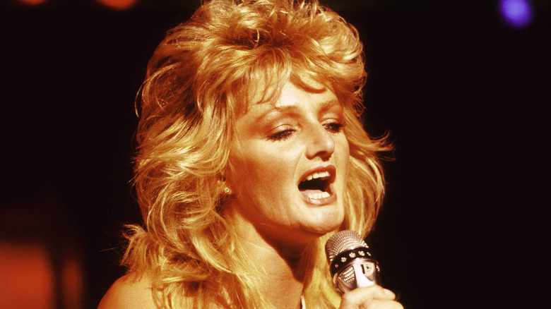 Bonnie Tyler singing into mic on stage in 1980s with big, blonde hair