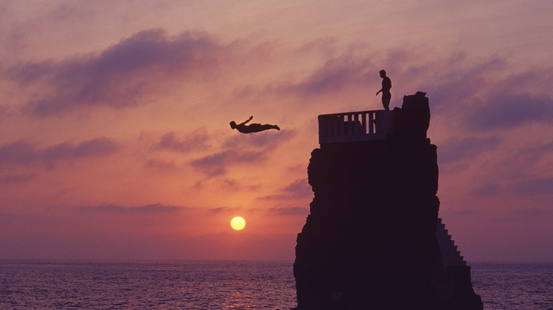 Man diving from cliff into water