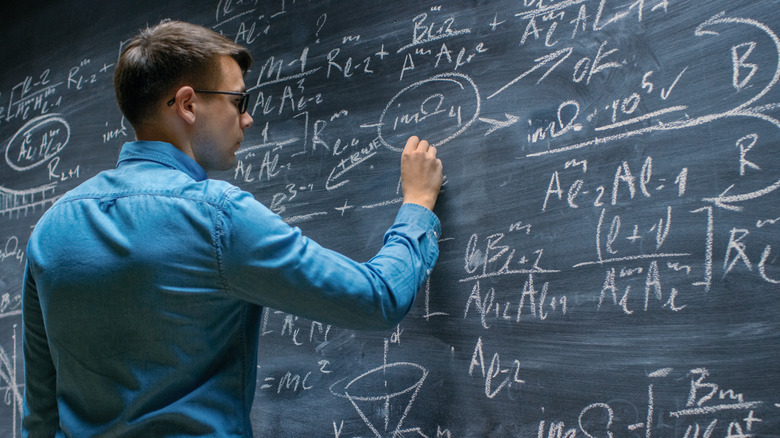 man writing equations on chalkboard