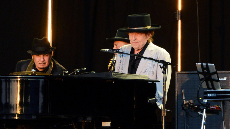 Bob Dylan on stage at piano in suit and hat
