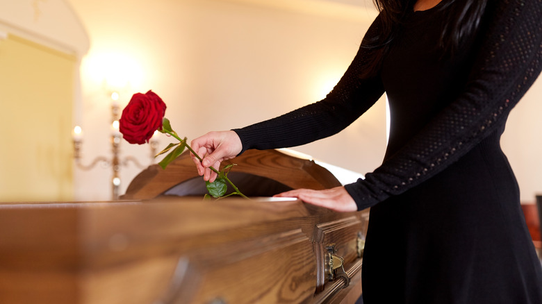 Woman dressed in black placing a rose on a coffin