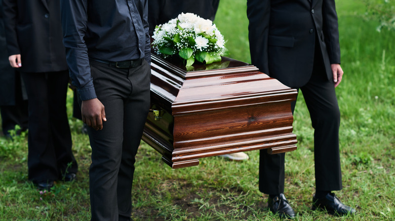 Pallbearers carrying casket topped with white flower bouquet