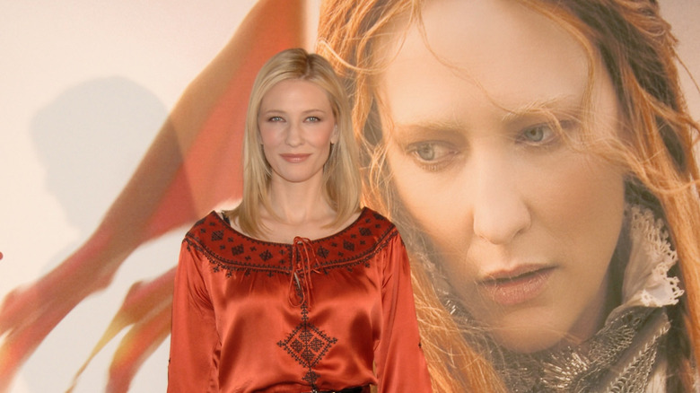 cate blanchett smiling in red shirt by poster for elizabeth the golden age