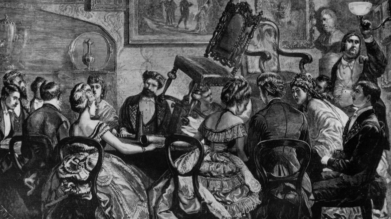 A couple of chairs hovering above a group of people during a seance-based after dinner entertainment