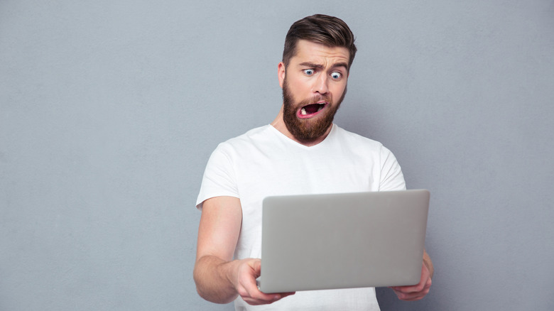 Man with an exaggerated stupid look on his face holding a laptop
