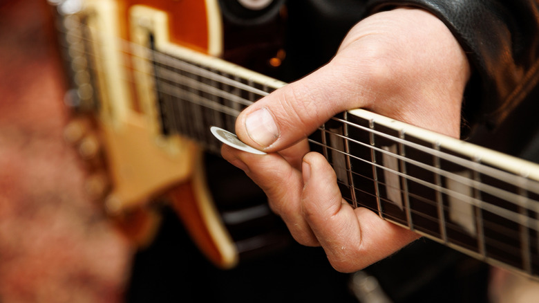 Person holding pick in front of a guitar