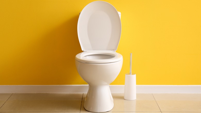 Open toilet by yellow wall