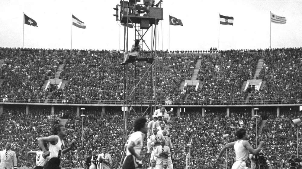 A photograph of runners at the 1936 Summer Olympics, with national flags at the top of the stadium.