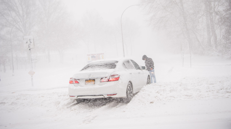 Man in hood by car in snowstorm