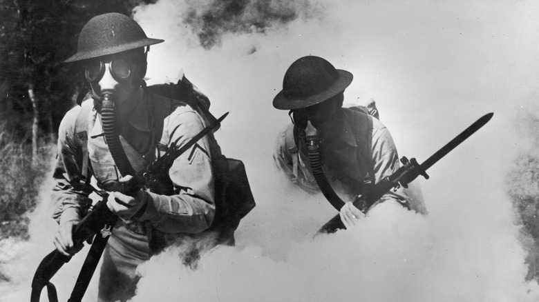 Two U.S. soldiers in WWI walk through smoke in gas masks