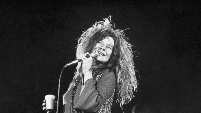 Janis Joplin performing live, smiling while singing into microphone