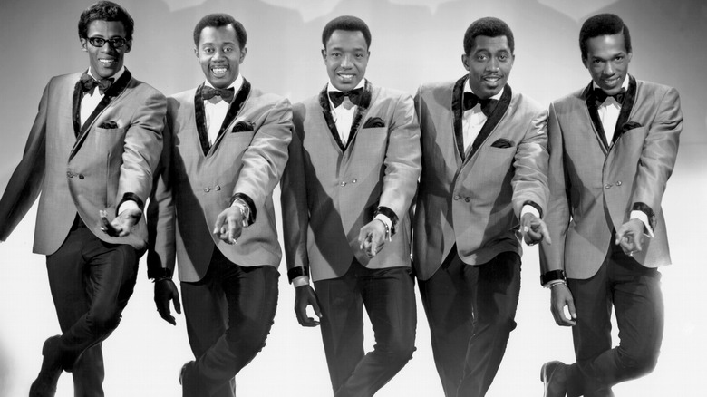 The Temptations dancing together smiling in suits