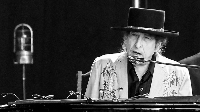 Bob Dylan wearing a hat and singing while sitting at a piano