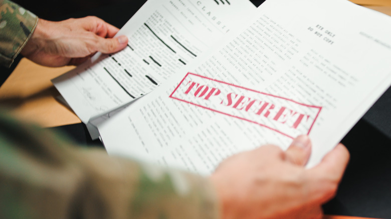 Sleeved hands holding documents labeled "top secret"