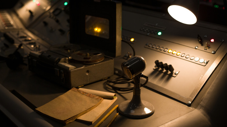 Vintage microphone on a control panel with buttons and toggle switches next to a notepad.