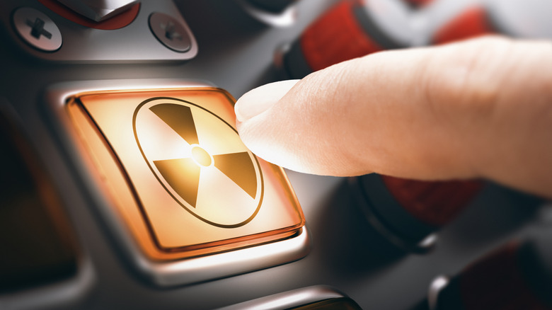 Finger pressing a nuclear button on a control panel, composite image.