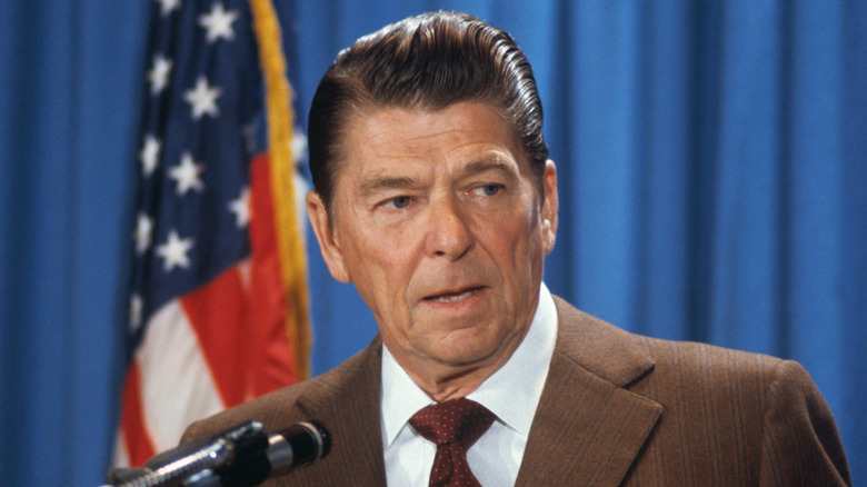 Ronald Reagan at microphone in front of flag looking away
