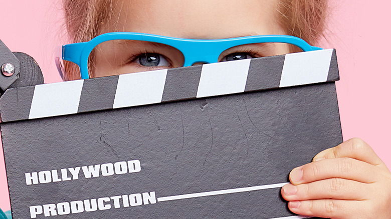Child in glasses holding clapperboard 