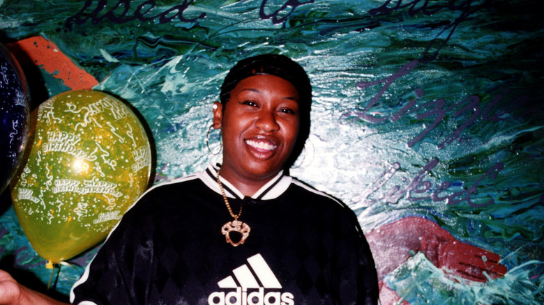 Missy Elliott in 1997 with short hair smiling against a mural