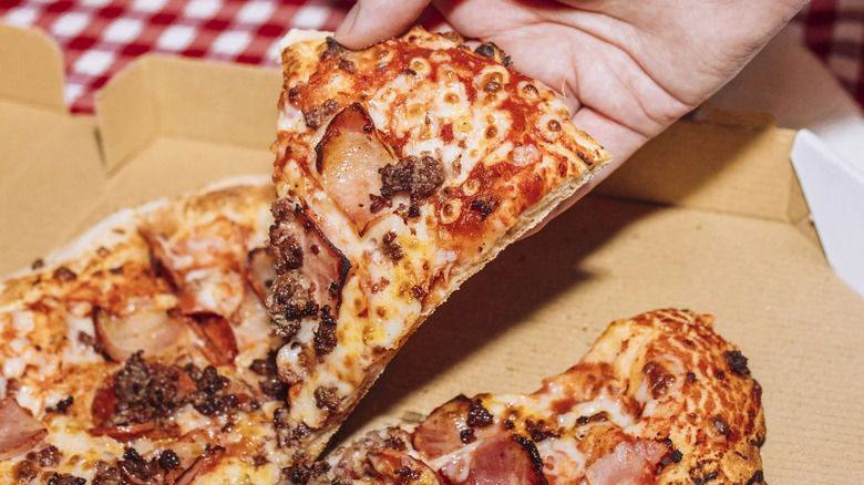 A hand grabbing a slice of pizza