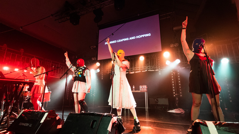 pussy riot in balaclavas performing on stage arms raised