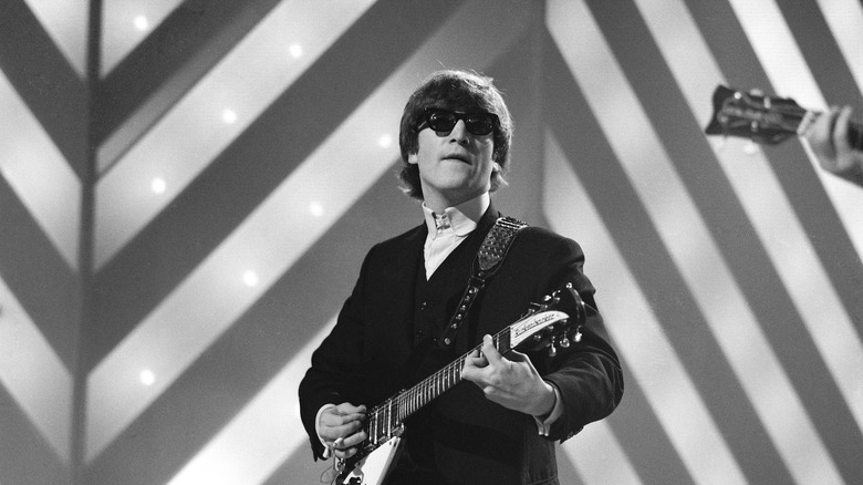 John Lennon in sunglasses playing guitar on stage