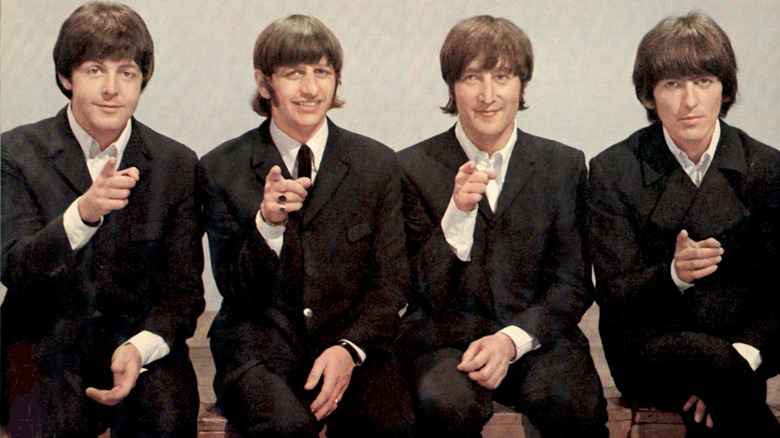 Paul McCartney, Ringo Starr, John Lennon, and George Harrison in black suits pointing ahead to the camera