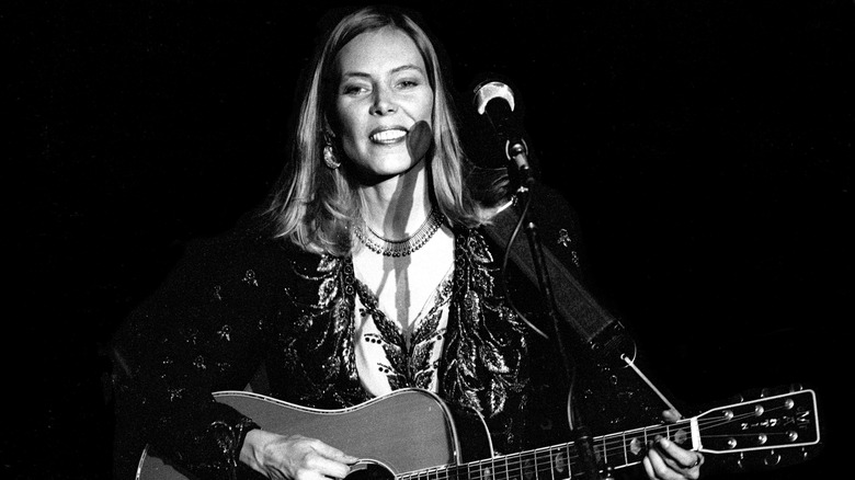 Joni Mitchell smiling playing the guitar on stage