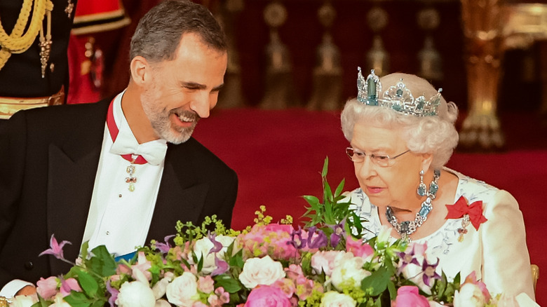King Felipe and Queen Elizabeth II laugh together in front of a floral arrangement