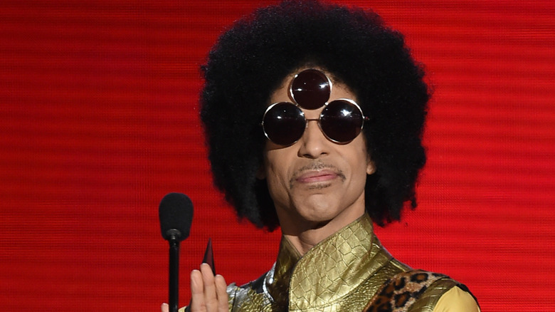 Prince with a gold collared shirt and sunglasses with three lenses