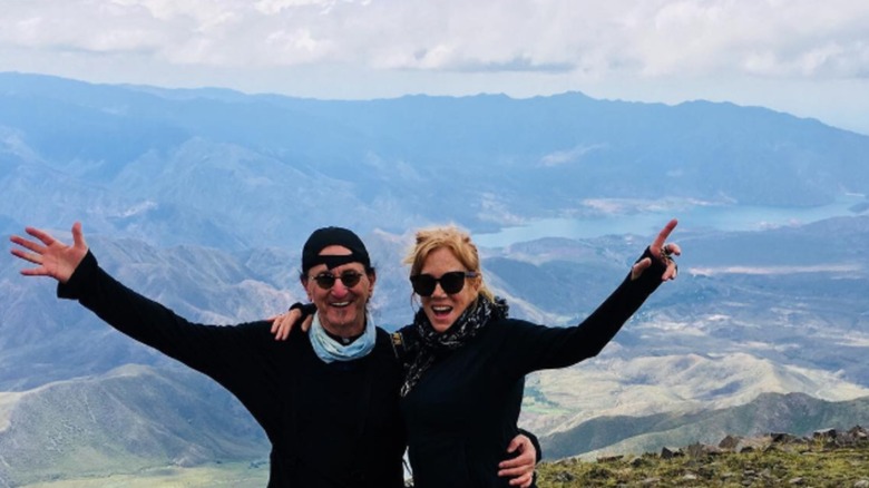 Geddy and Nancy Lee with arms in the air at the top of a mountain