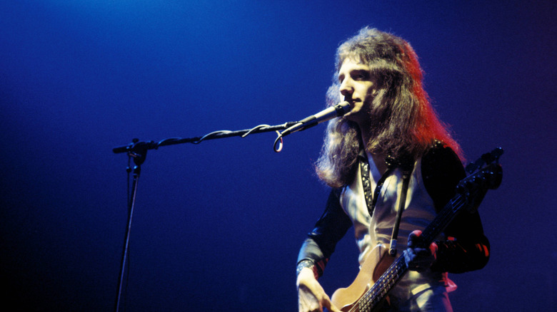 John Deacon singing and playing bass on stage