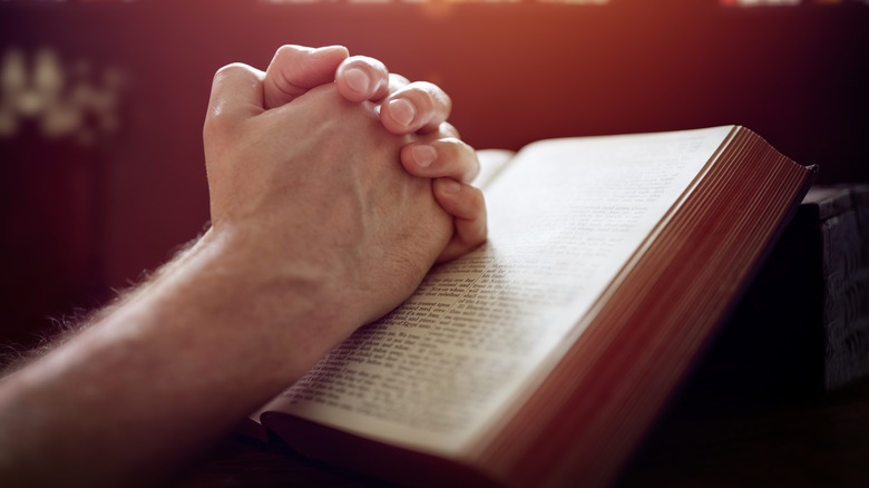 Man's hands clasped over an open bible.