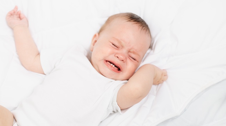 Baby in white onesie crying