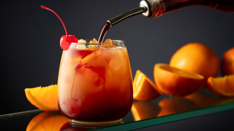 Syrup being poured into a tequila sunrise