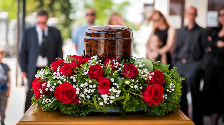 People standing behind an urn wrapped in red roses